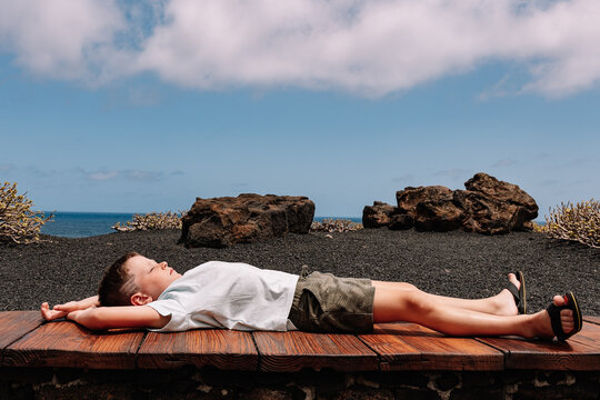 Serene kid lying on bench near sea