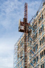 Construction crane beside building under construction with scaffolding against blue sky. © Kung37