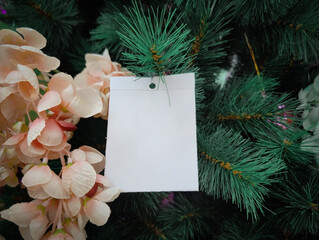 Paper card note for text copy space hangs on Christmas tree branches, and pink flower. Christmas, winter, new year concept. Close up.