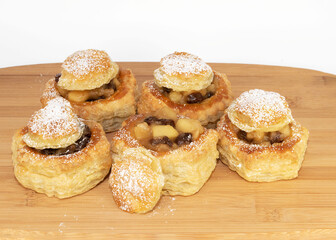 Apple and raisin stuffed puff pastry shells freshly baked are displayed on a wood board against a white background.