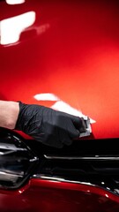Employee of a car wash or car detailing studio applies a ceramic coating to the paintwork of a red...