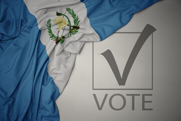 waving colorful national flag of guatemala on a gray background with text vote. 3D illustration