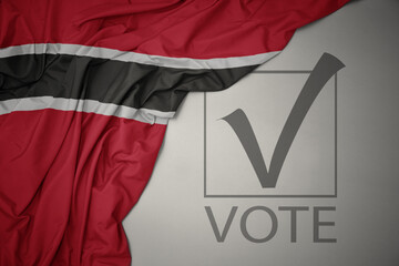 waving colorful national flag of trinidad and tobago on a gray background with text vote. 3D illustration