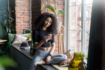 Multiethnic woman with African curls using smartphone at home or cafe indoors. Communication with friends of relatives. social media. Video photo content. Comfort relationships. Freelance