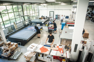 In a large modern printing plant, operators work on various types of machines for printed material