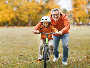 Fototapeta Happy family grandfather teaches child grandson  to ride a bike in park obraz