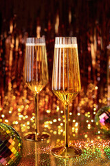 Champagne Flutes On Golden Sparkle Background With Mirror Balls. Celebration Christmas Romanic concept. Selective focus. Glasses of champagne against holiday lights.
