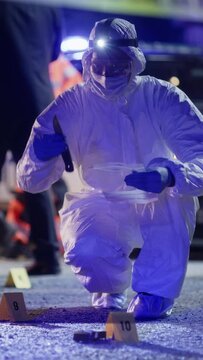 Vertical Shot: Forensics Specialist Picking a Bloody Knife From Crime Scene and Packing it as Evidence. Expert Checking Evidence Under Clear Lights, Considering Blood Patterns on Murder Weapon
