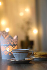 Plate with peanut butter cookies, cup of tea or coffee, open book, reading glasses and lit candles on the table. Selective focus.