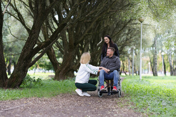 Happy disabled person in wheelchair and two women take care of him in park.