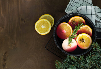 Mulled wine with pieces of orange and apples in a black ladle on a wooden background.