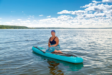 A woman with a Mohawk in a pareo on a SUP board in a lake against the background of white clouds on...