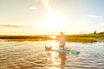 a man in shorts sits on a sup board at sunset in the water.