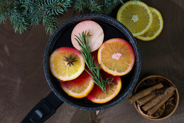 Mulled wine with pieces of orange and apples in a black ladle on a wooden background.