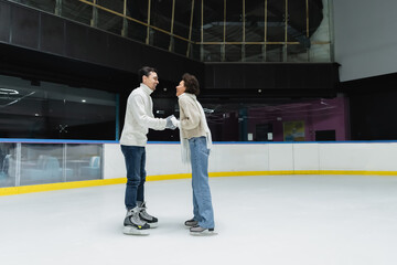 Side view of cheerful interracial couple spending time during date on ice rink