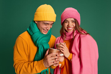 Portrait of young man and woman in bright knitted hat and scarf posing isolated over green background. Happiness and merry