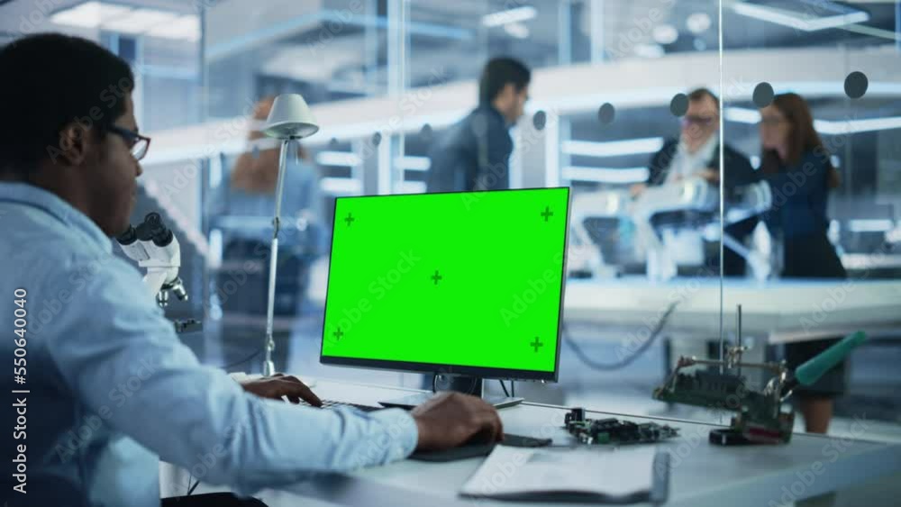 Poster Software Developer Working on Computer with Green Screen Mock Up Display. Scientific Lab, Engineering Research Center with Specialists Working on Mobile Robot Development in the Background.