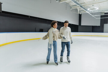 Young interracial couple holding hands while ice skating on rink