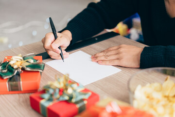 Close up man's hand is writing on a blank Christmas postcard with a pen. Couple sitting and writing Christmas card together for sending with surprise gifts at home during Christmas holiday.