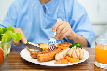 Asian senior or elderly old lady woman patient eating Salmon steak breakfast with vegetable healthy food while sitting and hungry on bed in hospital.