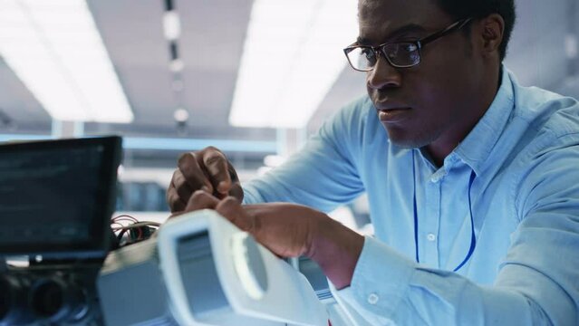 Close Up Portrait of an African American Robotics Engineer Setting Up a Robot Dog Prototype, Using a Screwdriver to Fasten the Bolts. Scientist Connect a Motherboard to a Mobile AI Four-Legged Robot.