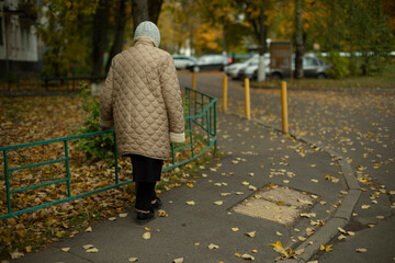 Pensioner walks down street in autumn. Old woman walks in city. Old woman walks path. Details of...