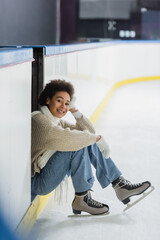 Smiling african american woman in ice skates looking at camera on rink
