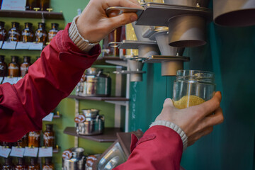 Adult client with glasses refilling a reusable jar with unpacked, organic and economic cereals in a local market commerce