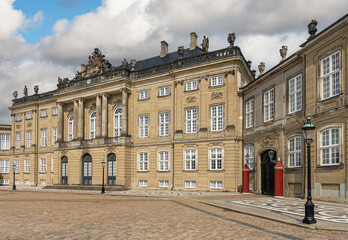 Fototapeta premium Copenhagen, Denmark - July 24, 2022: Brown stone Frederik VIII Palace and extra wing on Amalienborg under blue cloudscape. Brown stones with pediment statues, columns and classical architecture