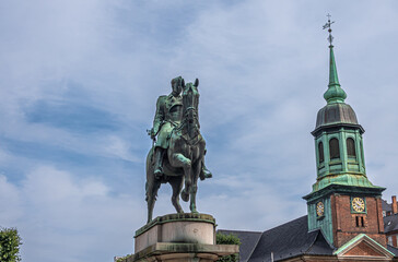 Fototapeta na wymiar Copenhagen, Denmark - July 24, 2022: Closeup of King Christian X equestrian greenish bronze statue on beige stone pedestal at Saint Anna square under blue cloudscape