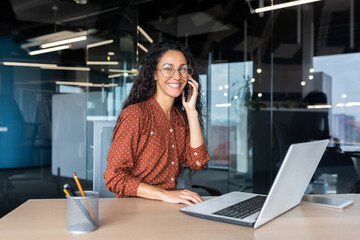 Portrait of successful latin american business woman, office worker smiling and talking on phone...