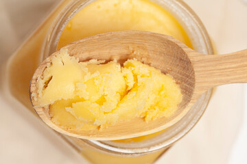 Ghee in jar and wooden spoon isolated on white background
