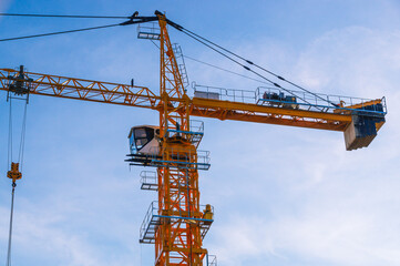 A tower construction crane on the background of a blue sky with clouds. Boom rotary crane with boom. Construction of apartment buildings in the city. Construction of high-rise buildings.