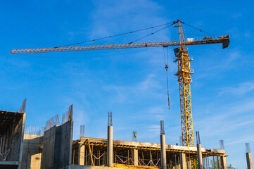 A tower construction crane on the background of a blue sky with clouds. Boom rotary crane with boom. Construction of apartment buildings in the city. Construction of high-rise buildings.