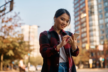 Young Asian student texting on her smart phone in city. - obrazy, fototapety, plakaty
