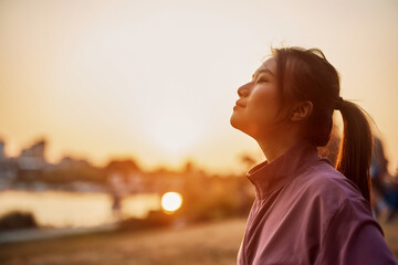Young Asian athletic woman enjoys in sunset with her eyes closed.