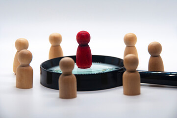 Obraz premium Red wooden doll on top of magnifying glass surrounded with other wooden figure. leadership concept
