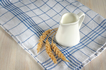 A small jug of cream or milk on a white, blue-checked cloth napkin. Natural lighting, selective focus