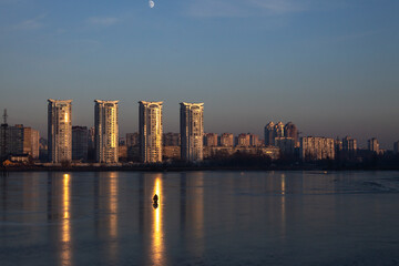 Obraz premium Fisherman on the frozen lake with skyscrapers in the background at the dusk