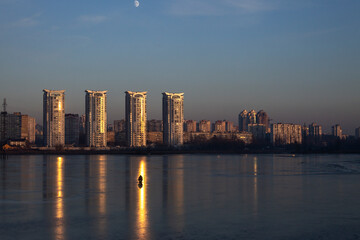 Fisherman on the frozen lake with skyscrapers in the background at the dusk