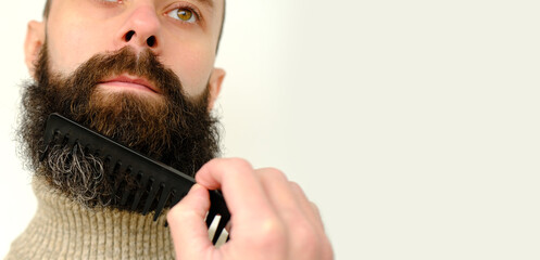 close-up of male face, young bearded and mustachioed man, guy with 25 - 30 years combs his thick beard, concept of mustache and beard stubble care products, hairline hygiene on lower part of face