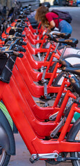 Detail of the handlebars and pedals of shared rental red bicycles parked in a row on a street in the city of Barcelona.