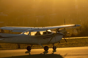 A small propeller plane rolling down the runway in backlight under a yellow sunset sun