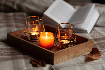 warm cozy bedroom winter or autumn concept, candles on tray and a book