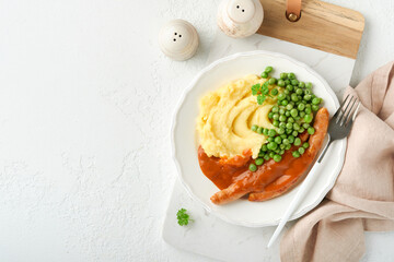 Bangers and mash. Grilled sausages with mash potato and green pea on white plate on light background. Traditional dish of Great Britain and Ireland. BBQ beef sausages. Top view.