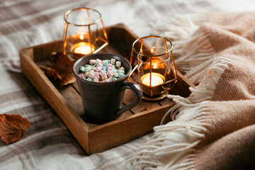 warm cozy bedroom winter or autumn concept, cup of hot chocolate on tray, candles throw