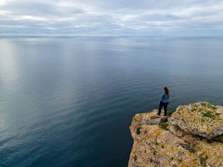Person on cliff standing looking towards the horizon.