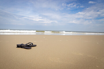 Fototapeta na wymiar lonely sandals on the beach with a cloudy sky in summer