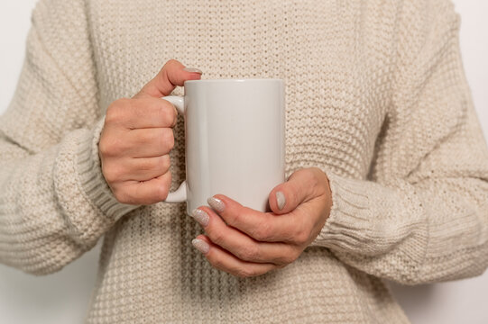 A woman in a white jumper is holding a white mug. The concept of comfort and warmth.