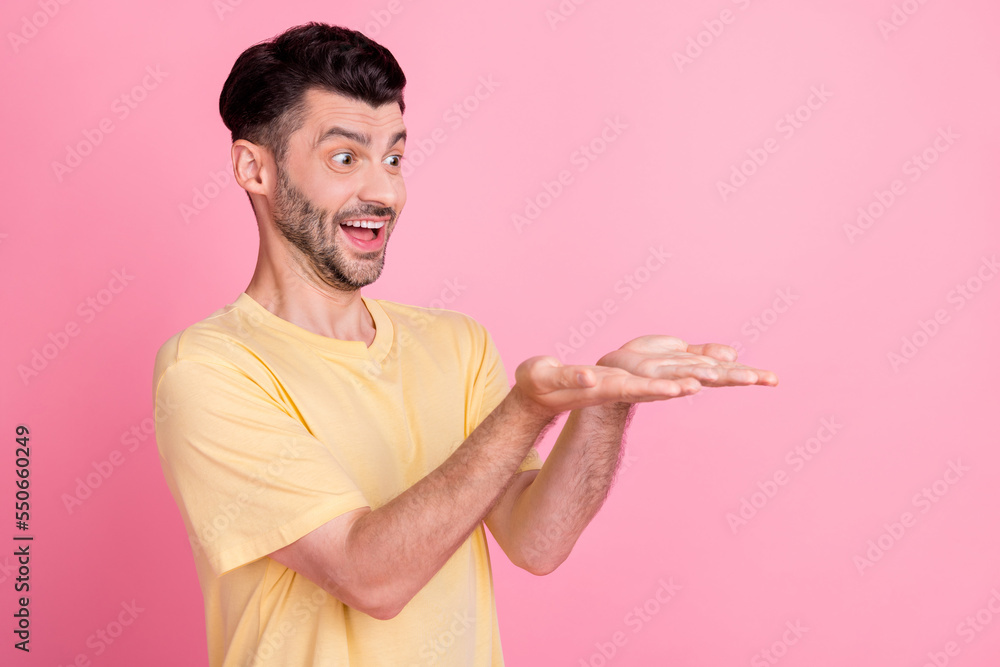 Poster portrait of crazy impressed positive man wear yellow t-shirt look at palms directing empty space iso